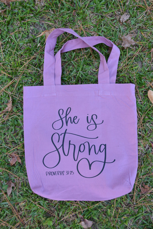 Purple Christian tote bags displaying, She is strong Proverbs 31:25